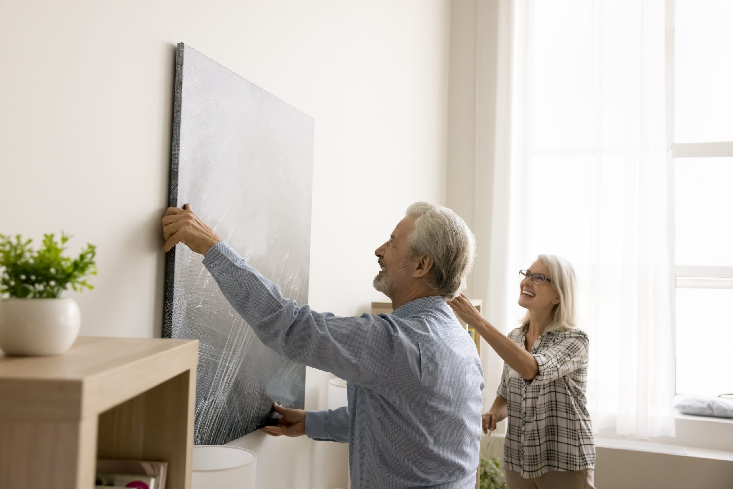 Cheerful senior couple decorating apartment, hanging large picture